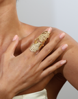 Close-up of a hand wearing a gold ring with intricate design on a neutral background