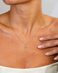 Gold necklace with a pendant worn by a person, with a hand touching the chest.