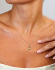Gold necklace with a pendant worn by a person, with a hand touching the shoulder.