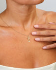 Necklace with a small pendant worn by a person, with a hand touching the chest.