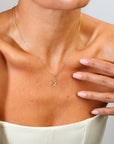 Necklace with a 'S' pendant worn by a person, with a hand touching the chest.
