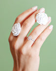 Hand wearing two white rose rings and a diamond ring on a green background
