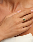Close-up of a hand wearing a gold ring with a green gemstone on a blurred background