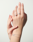 Two hands wearing silver rings and a bracelet on a light gray background