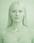 Woman wearing a gold necklace with a nameplate against a light green background