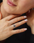 Close-up of a woman's hand wearing a ring with a black stone, against a blurred background.