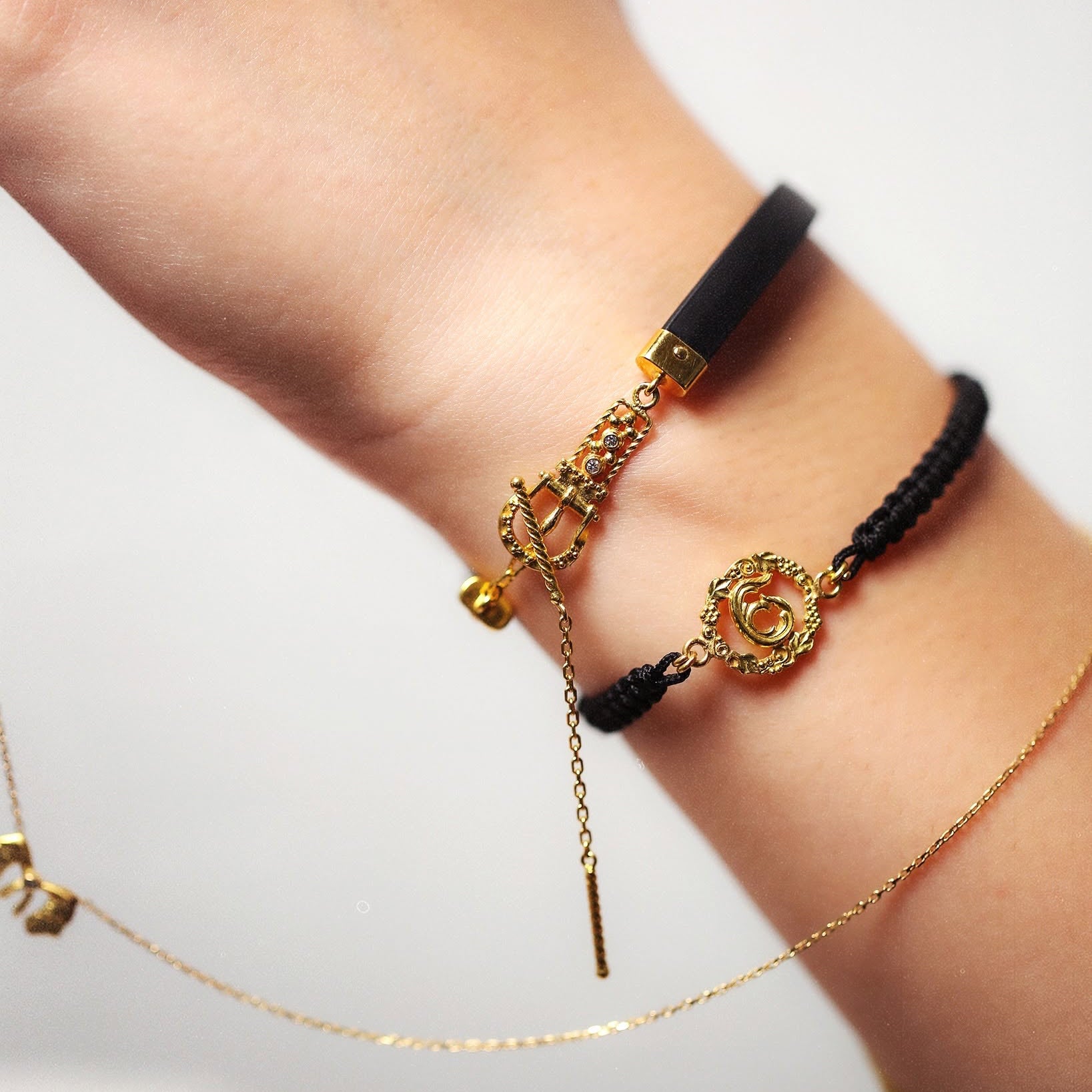 Close-up of a wrist wearing gold and black bracelets with a visible brand logo.