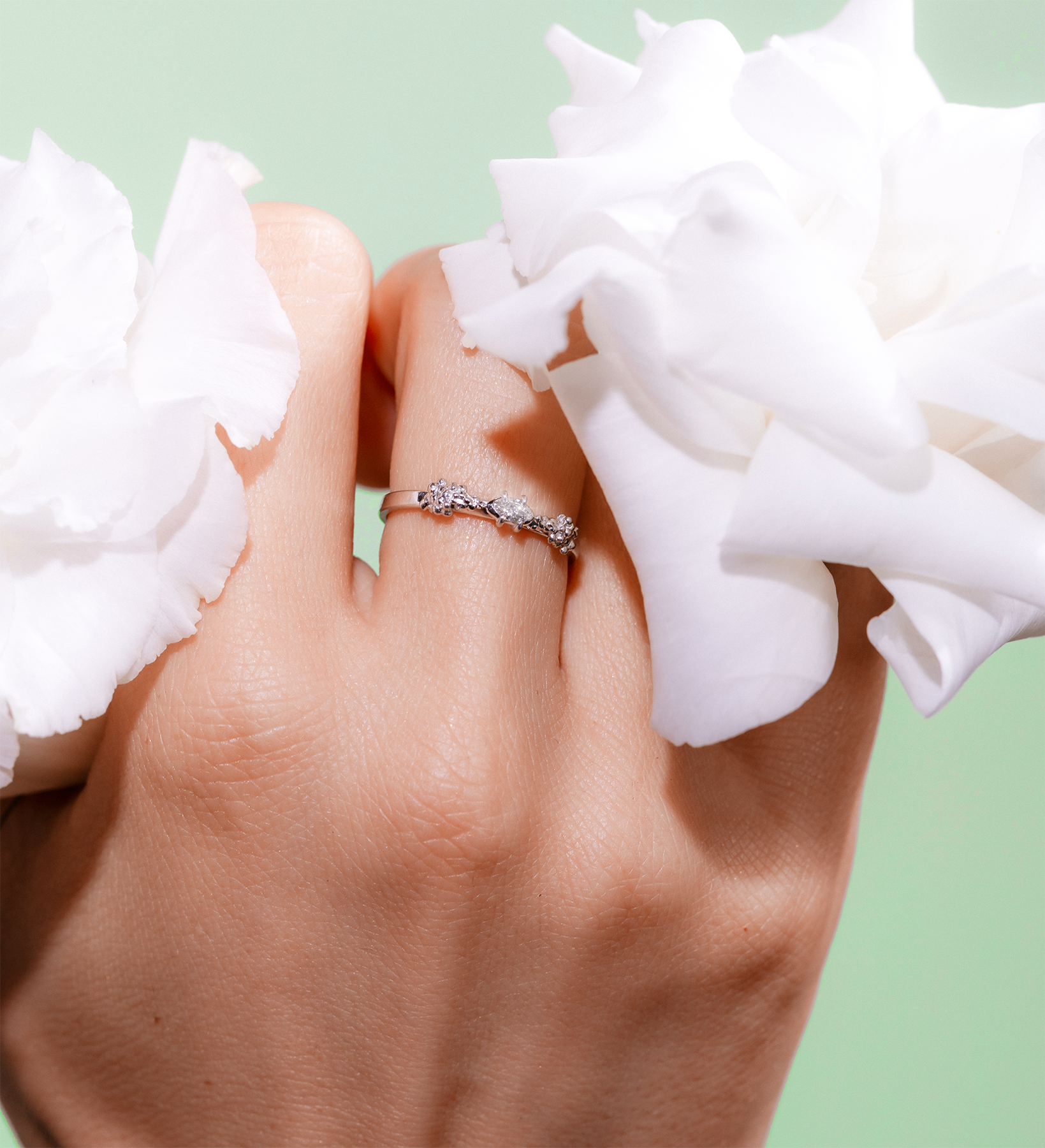 Hand wearing a ring with white flowers on a light green background
