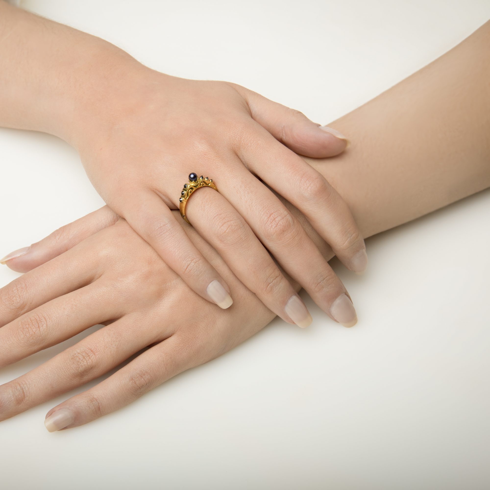 Close-up of a hand wearing a gold ring with a black gemstone on a white background