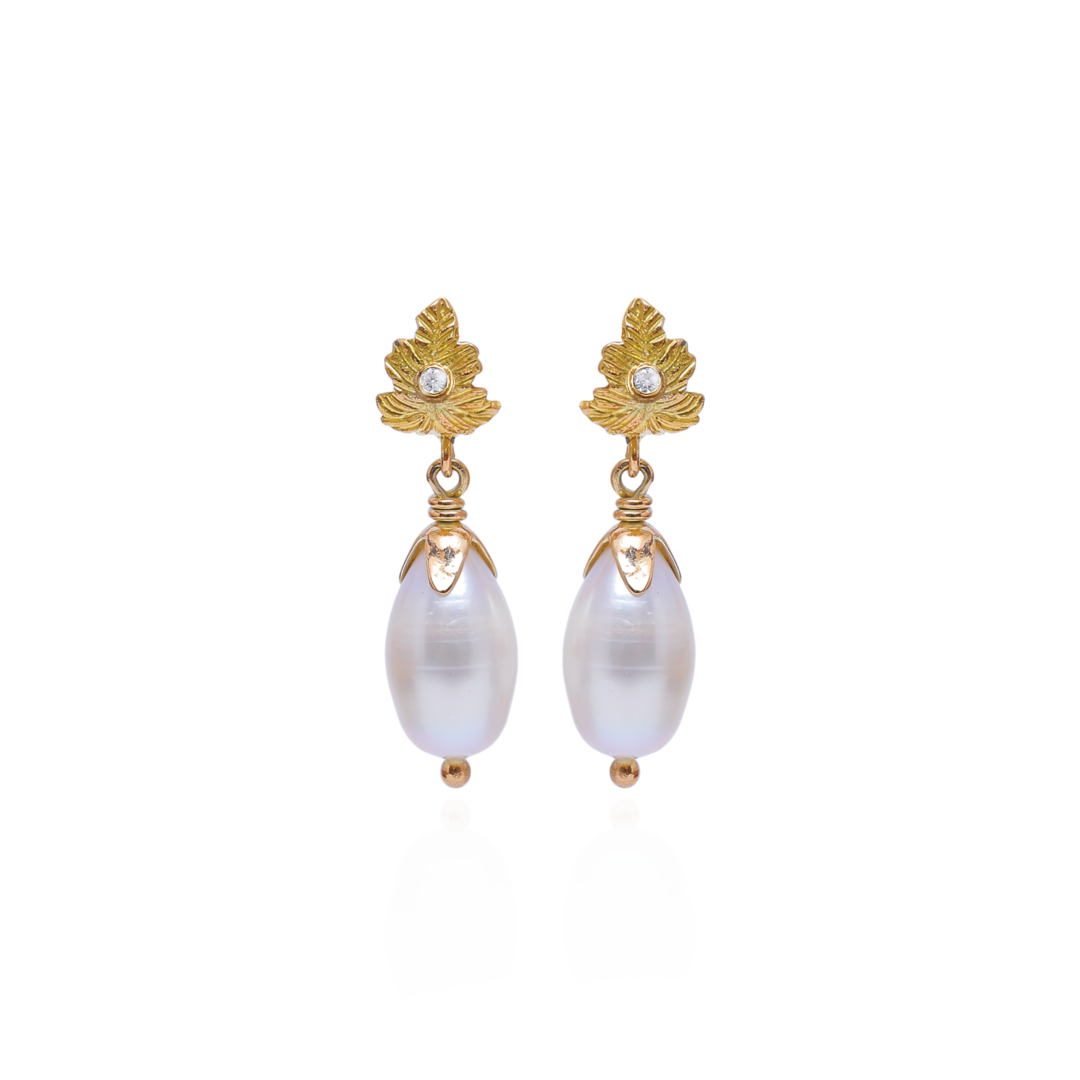 Gold earrings with leaf designs and pearl-like beads on a white background