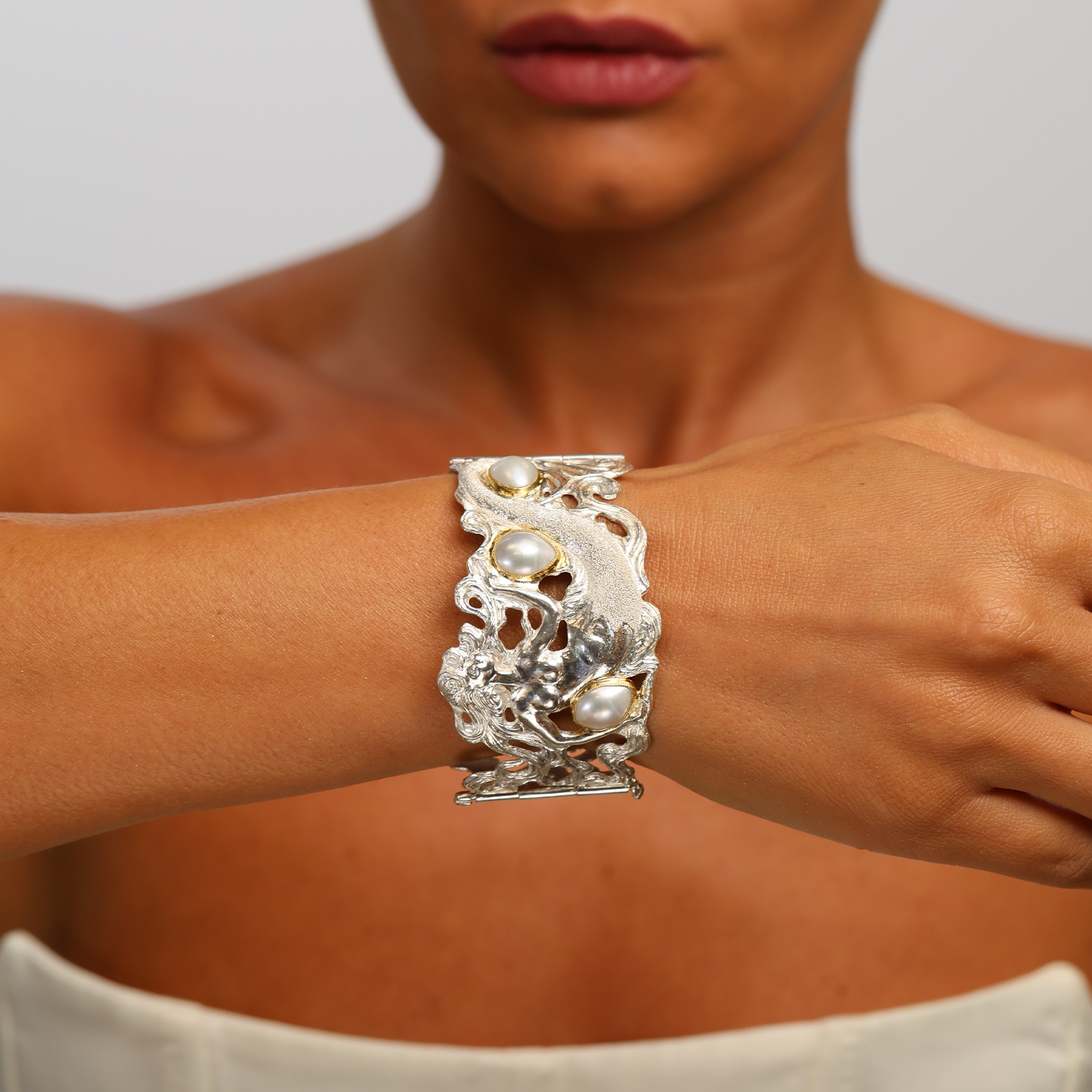Close-up of a person wearing a decorative silver bracelet with pearls on a neutral background