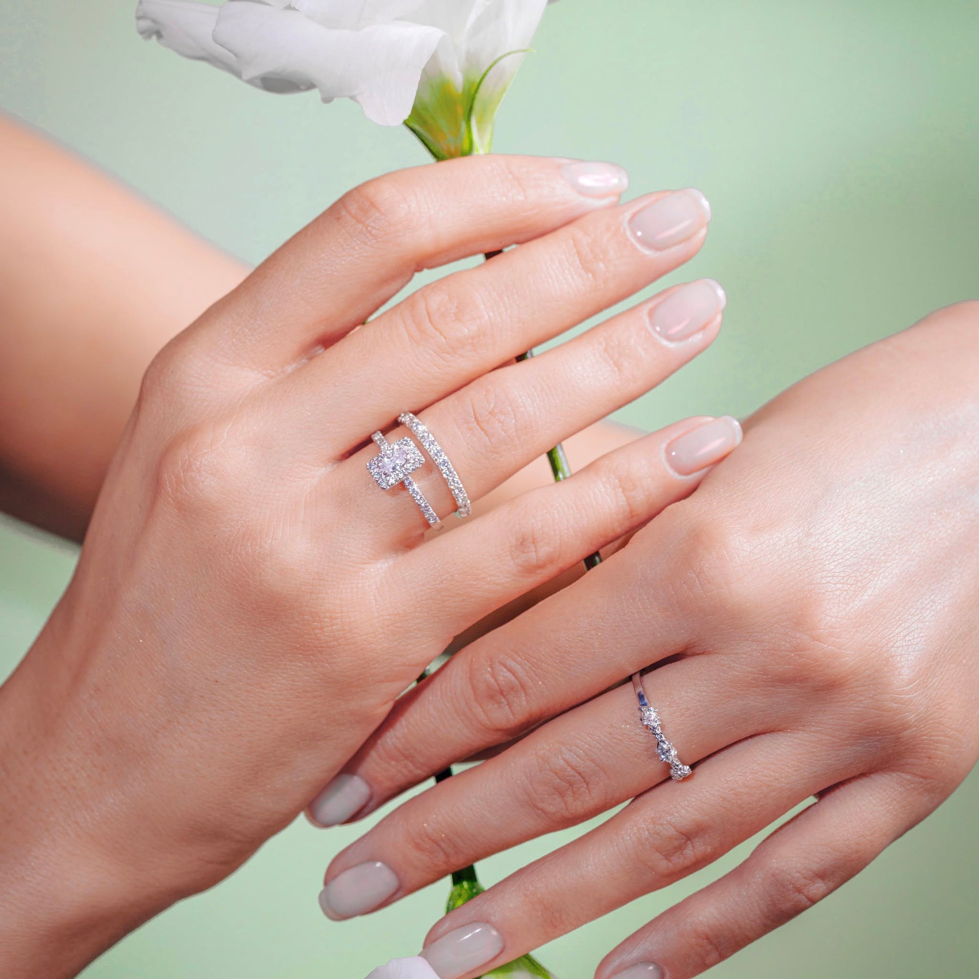Two hands wearing diamond rings with a light green background