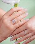 Two hands wearing diamond rings with a light green background