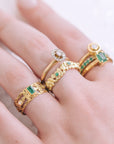Close-up of a hand wearing gold rings with emeralds and diamonds.