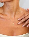 Woman wearing a gold necklace with a small pendant on a neutral background