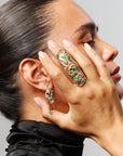 Woman wearing gold and green gemstone jewelry on a gray background
