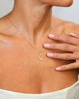 Gold necklace with a 'C' pendant worn by a person, with a hand touching the chest.