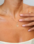 Gold necklace with a 'G' pendant worn by a person, with a hand touching the chest.