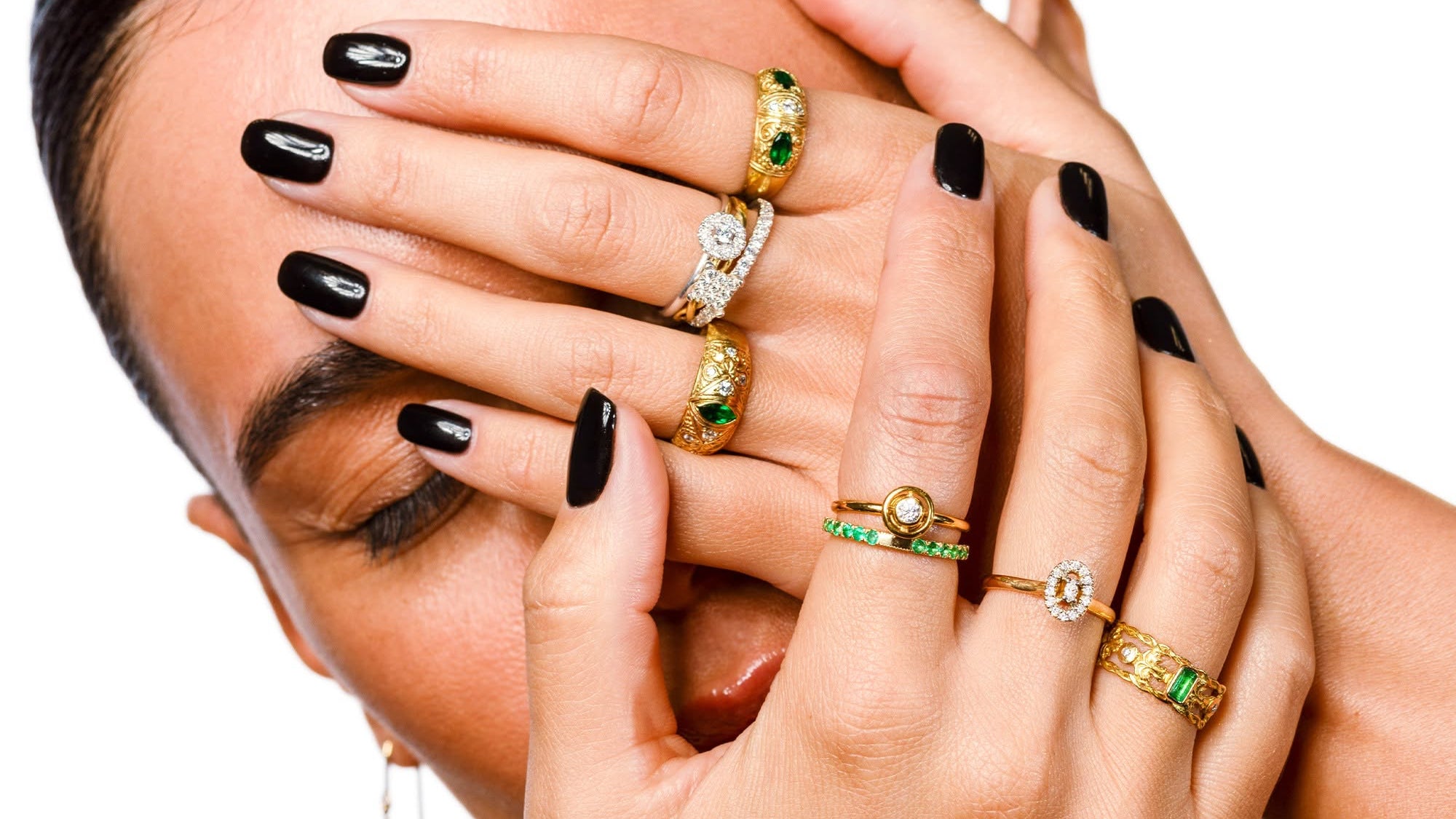 Woman's hands with multiple gold and gemstone rings on a white background
