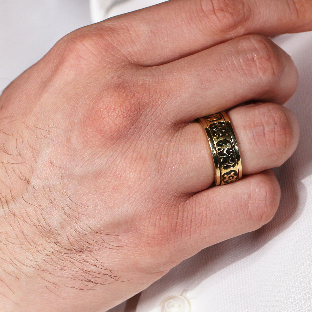 Gold ring with intricate design on a person's finger against a white background