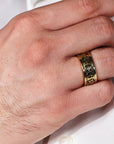 Gold ring with intricate design on a person's finger against a white background
