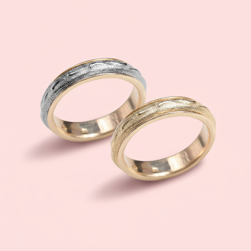 Two gold rings with textured band design on a pink background