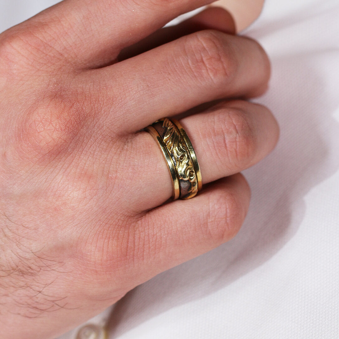 Hand wearing a gold ring with intricate design on a light background