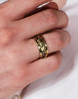 Hand wearing a gold ring with intricate design on a light background
