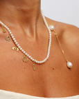 Pearl necklace with gold charms on a person against a neutral background