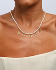Pearl necklace with gold charms on a person wearing a white top against a light background