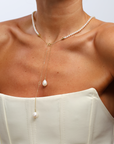 Pearl necklace with a pendant on a person wearing a white top against a light gray background