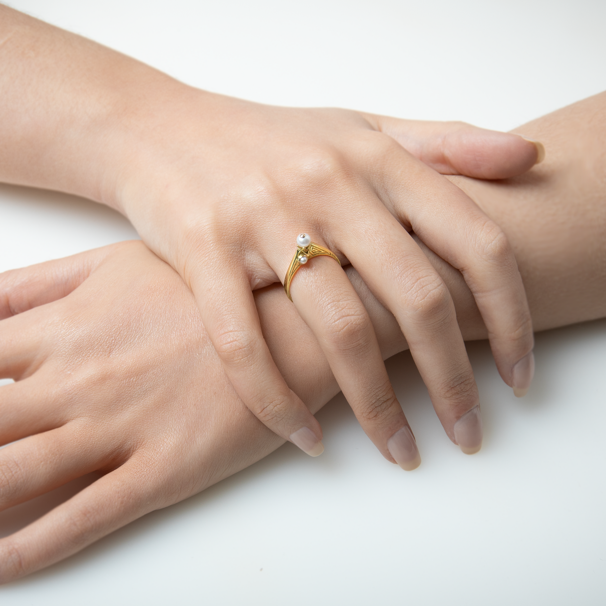 Close-up of hands with a gold ring featuring a pearl on a white background