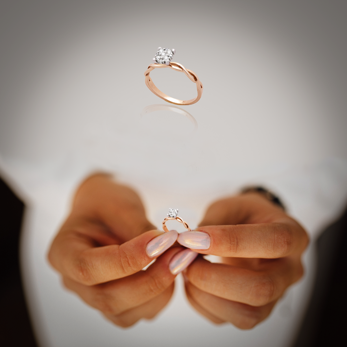 Rose gold ring with a diamond held between two fingers against a neutral background