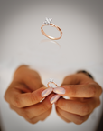 Rose gold ring with a diamond held between two fingers against a neutral background