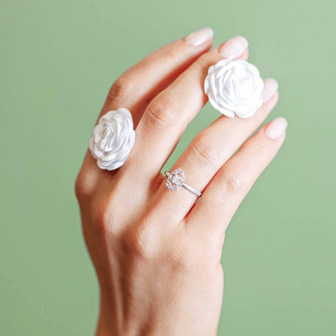 Hand wearing two white rose rings and a diamond ring on a green background