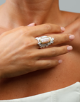Close-up of a hand wearing an ornate ring with a large central gemstone, set against a neutral background.