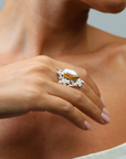 Close-up of a hand wearing a ring with a large pearl on a neutral background