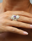 Hand wearing a silver ring with a purple gemstone against a neutral background