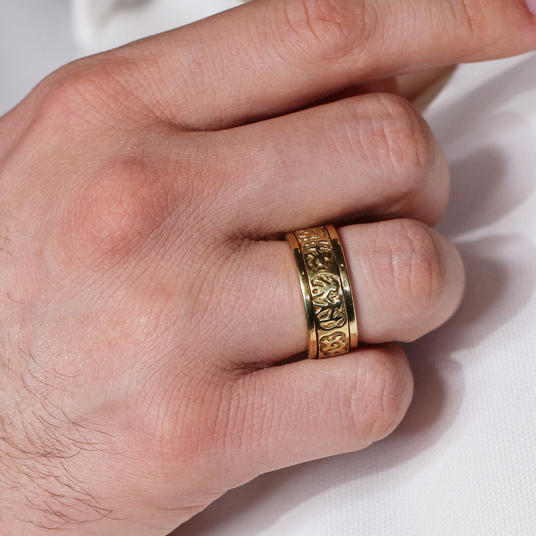 Gold ring with intricate design on a finger against a white background