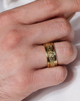 Gold ring with intricate design on a finger against a white background