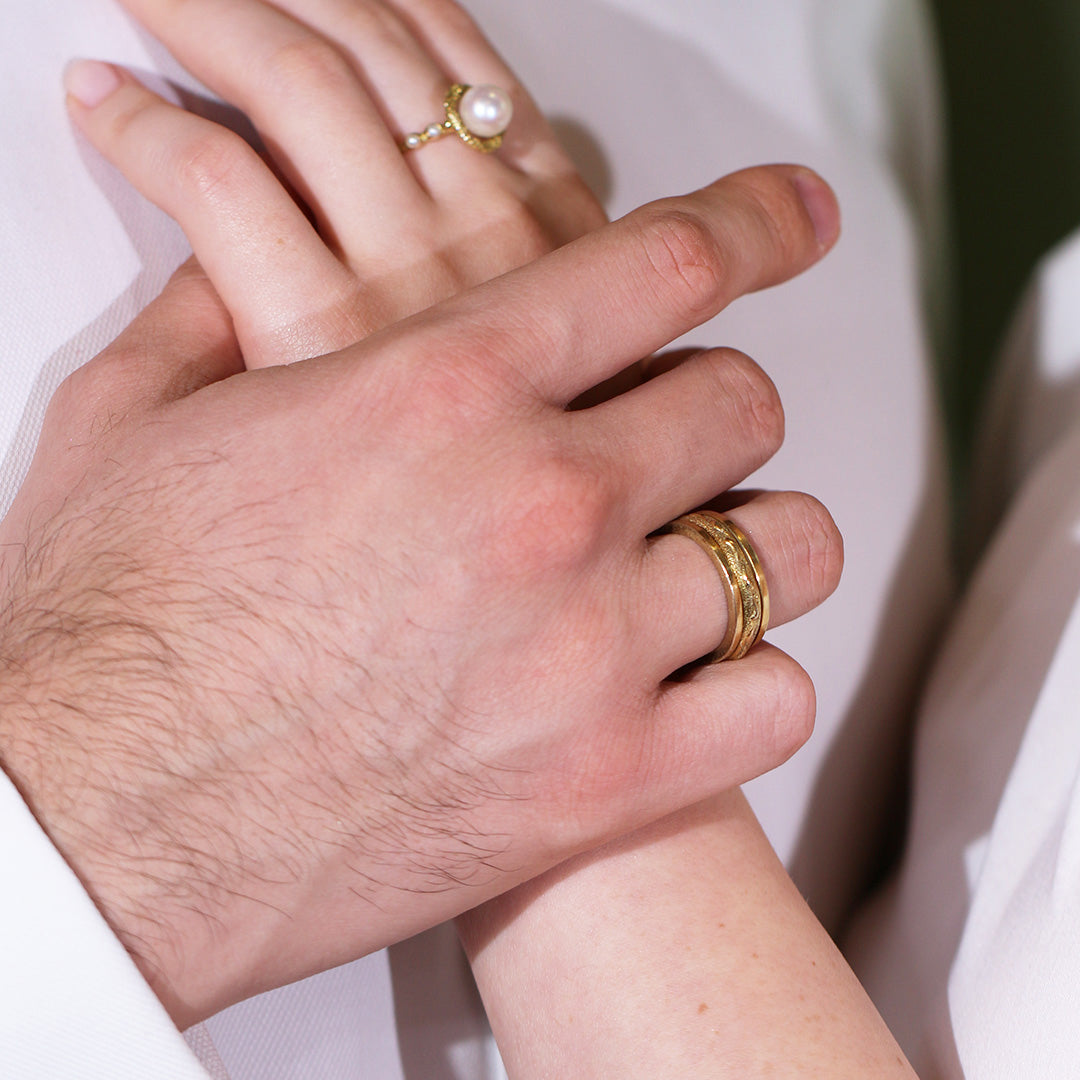 Close-up of two hands with gold rings on a light background