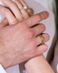 Close-up of two hands with gold rings on a light background